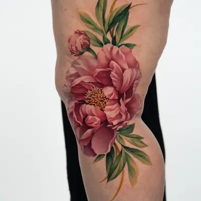 Color tattoo on the side of the left knee: a large open pink peony with a bud and green leaves, stems running above and below the knee.