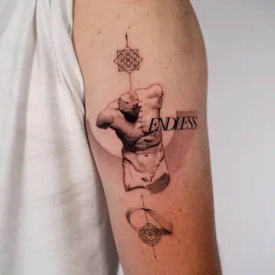 Black and grey fine-line tattoo on the back of a man's upper arm: a classical marble statue torso with the word ENDLESS set across it, a soft grey half-circle behind, and two geometric sacred-geometry marks on a vertical line above and below, the lower one wrapped by a Möbius strip.