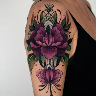 Color neo-traditional tattoo on the outer upper arm and shoulder cap: a symmetrical stack of deep plum peonies with green leaves, a pale jewel-like center spine, black filigree and dotwork, ending in a dotted point above the elbow.