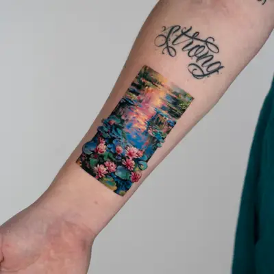Color painterly tattoo on the inner forearm: a rectangular rendering of Monet's water lily pond at sunset, with pink and orange reflections on blue water and pink water lilies and pads along the bottom breaking past the edge of the frame.