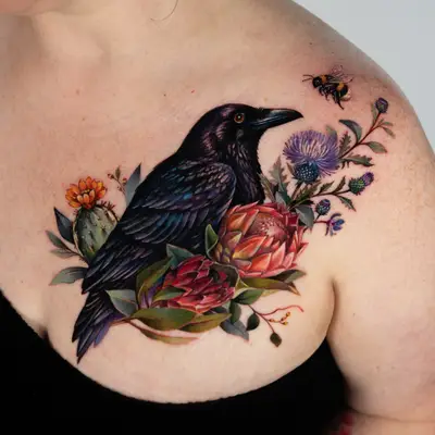 Color realism cover-up across the upper chest and collarbone toward the shoulder: an iridescent black crow with an orange eye among pink and red protea, a flowering prickly pear cactus, purple thistles and eucalyptus leaves, with a bumblebee near the shoulder.