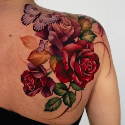 Color tattoo on the right shoulder blade of deep red and burgundy roses with green and amber leaves, two lilac butterflies near the top, and thin stems sweeping down toward the arm.