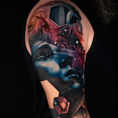 Color tattoo on the upper arm of a serene blue-toned face tilted upward into a red and purple nebula with a spiral galaxy and stars, the Voyager probe framed in a hexagonal window above, and hexagonal panels and an asteroid field below.