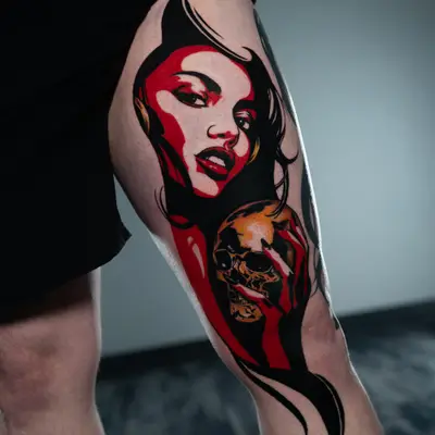 Tattoo of a woman's face with a skull, colored in red and black, on a leg.