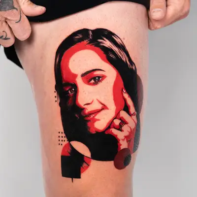 Red-and-black Portrait tattoo with abstract shapes on thigh