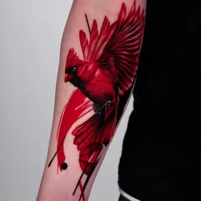 Red cardinal tattoo with black abstract elements on the forearm.