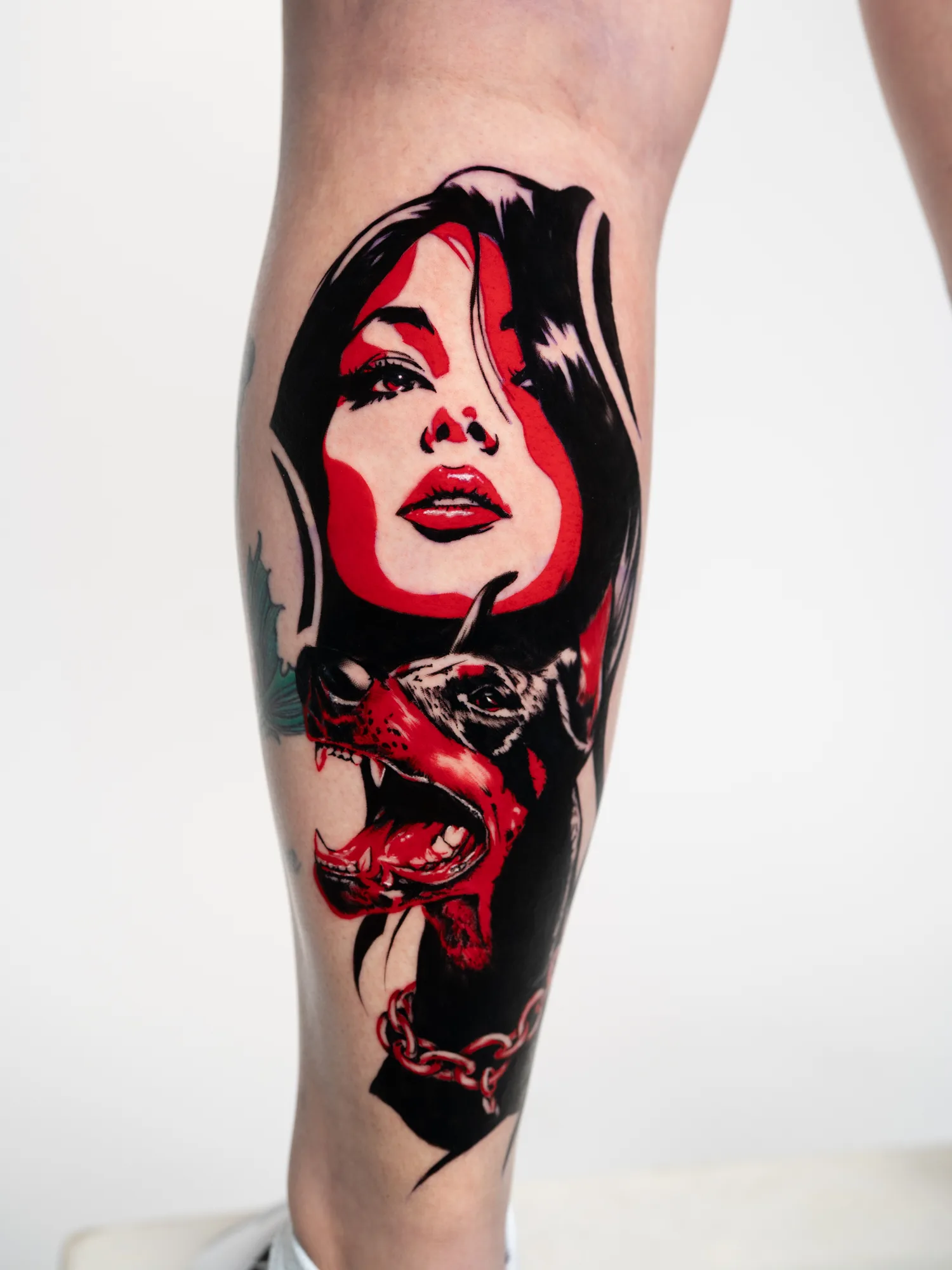Tattoo of a woman's face and a growling dog in black and red ink.