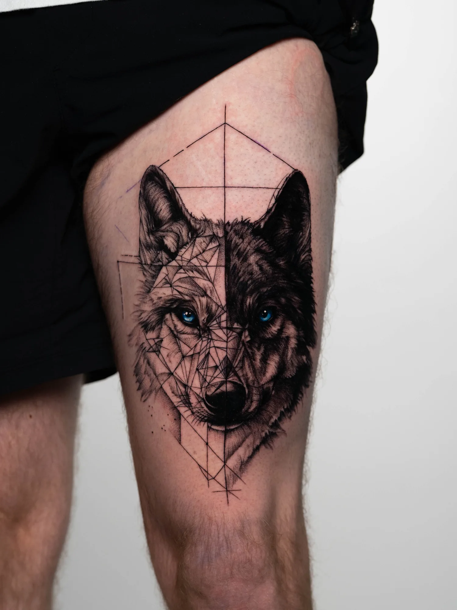 Geometric wolf tattoo with blue eyes on upper thigh.