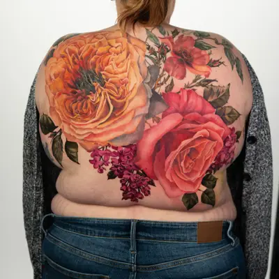 Colorful floral tattoo on a woman's back featuring roses and vines.