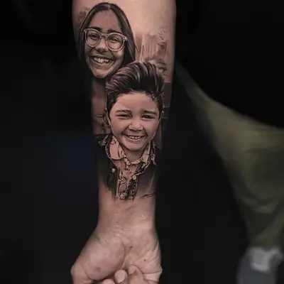 Realistic portrait tattoo of two smiling children on an arm.