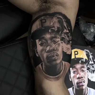 Realistic portrait tattoo on a thigh, showing a man in a cap with smoke around him.