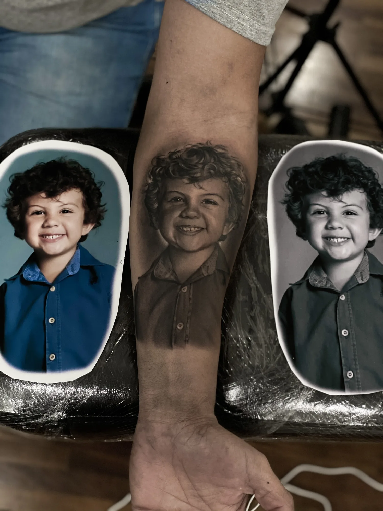 Black and grey portrait tattoo of a young child on forearm.