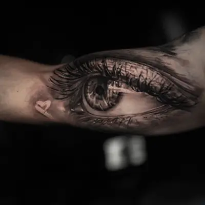 Realistic eye tattoo on inner arm with detailed eyelashes.