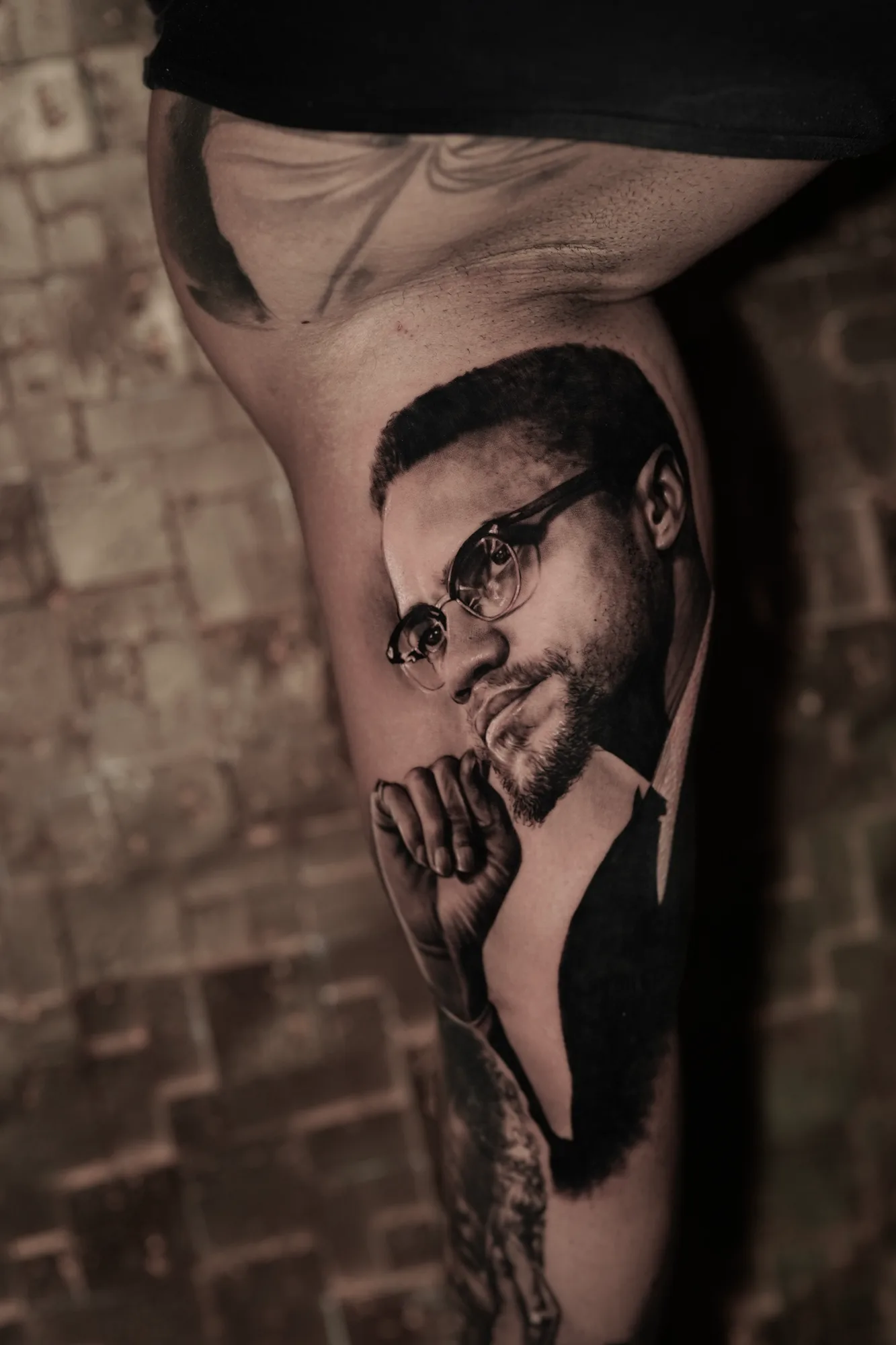 Black and grey realistic portrait tattoo of a man with glasses and beard.