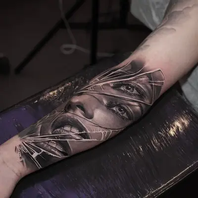 Forearm tattoo of fragmented woman's face with focus on eyes and mouth.