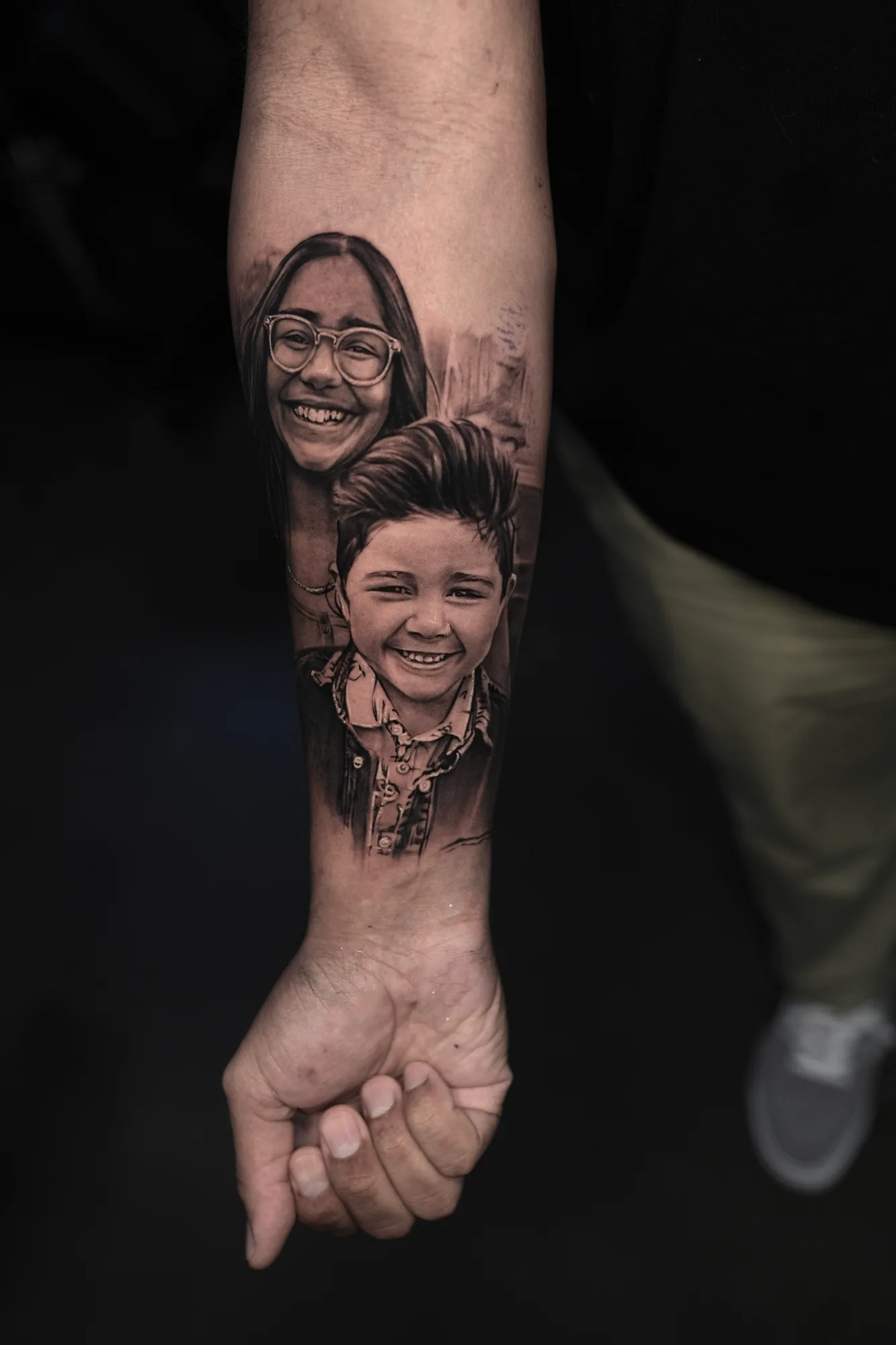 Realistic portrait tattoo of two smiling children on forearm.