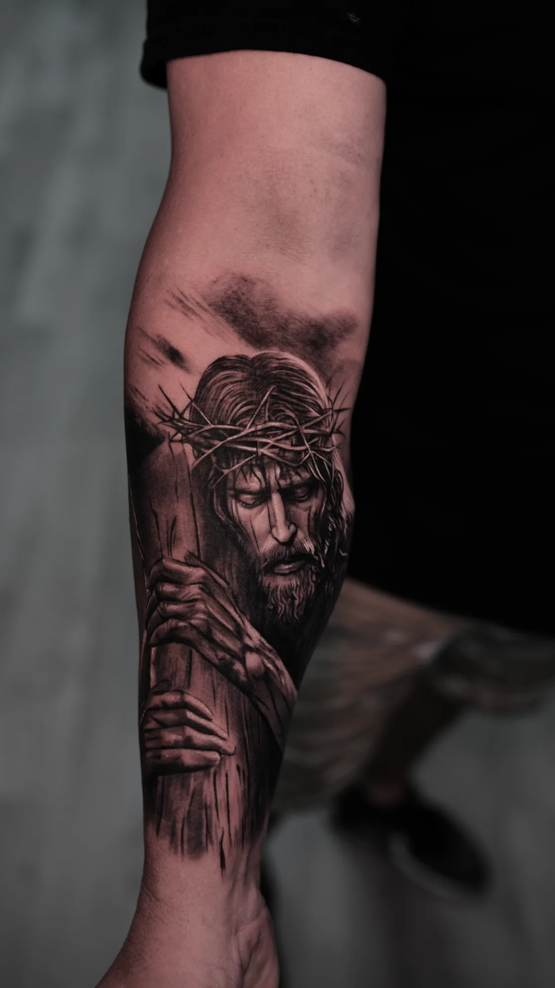 Black and grey tattoo of Jesus with crown of thorns on forearm.