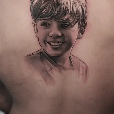 Portrait tattoo of a smiling child on a person's back.