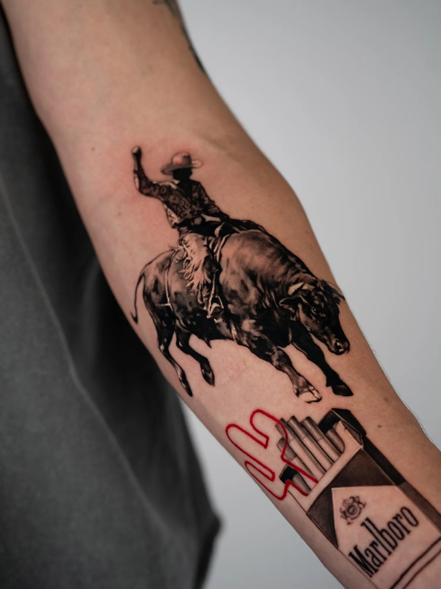 Tattoo of a cowboy riding a bull next to a Marlboro cigarette pack.