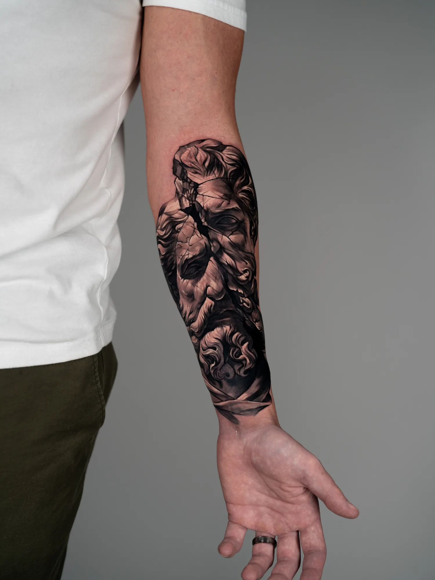 A detailed black and grey tattoo on a forearm featuring a cracked face with elaborate hair.