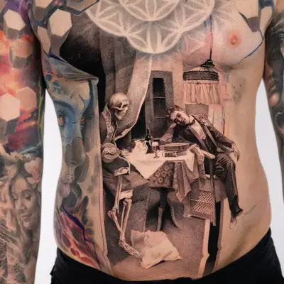 Black and grey stipple tattoo across a stomach showing a skeleton seated at a dinner table with a man in a suit slumped back in his chair, a hanging lamp above and a sacred geometry pattern across the chest.