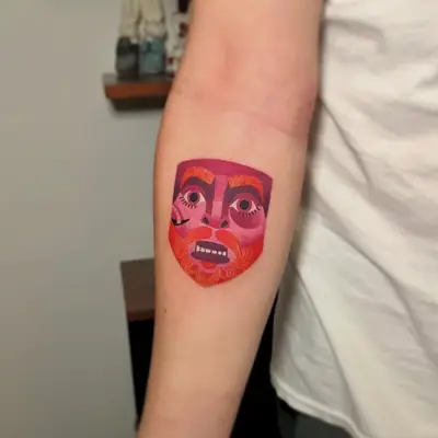 Tattoo of a colorful abstract face on inner forearm.