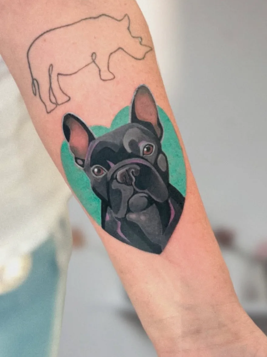 Tattoo of a French bulldog head with a teal heart background on forearm.