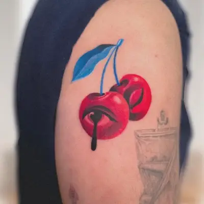 Colorful tattoo of two cherries with an eye design on upper arm.