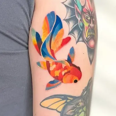 Colorful goldfish tattoo with adjacent demon face and insect designs.