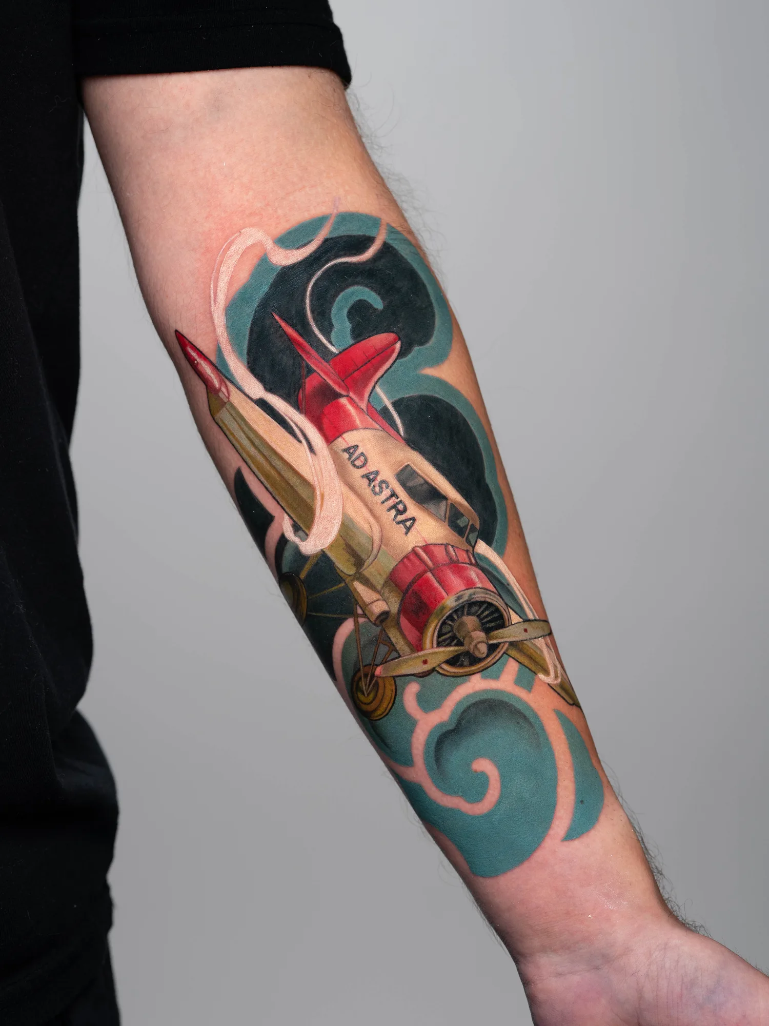 Tattoo of red airplane with 'Ad Astra' banner on arm