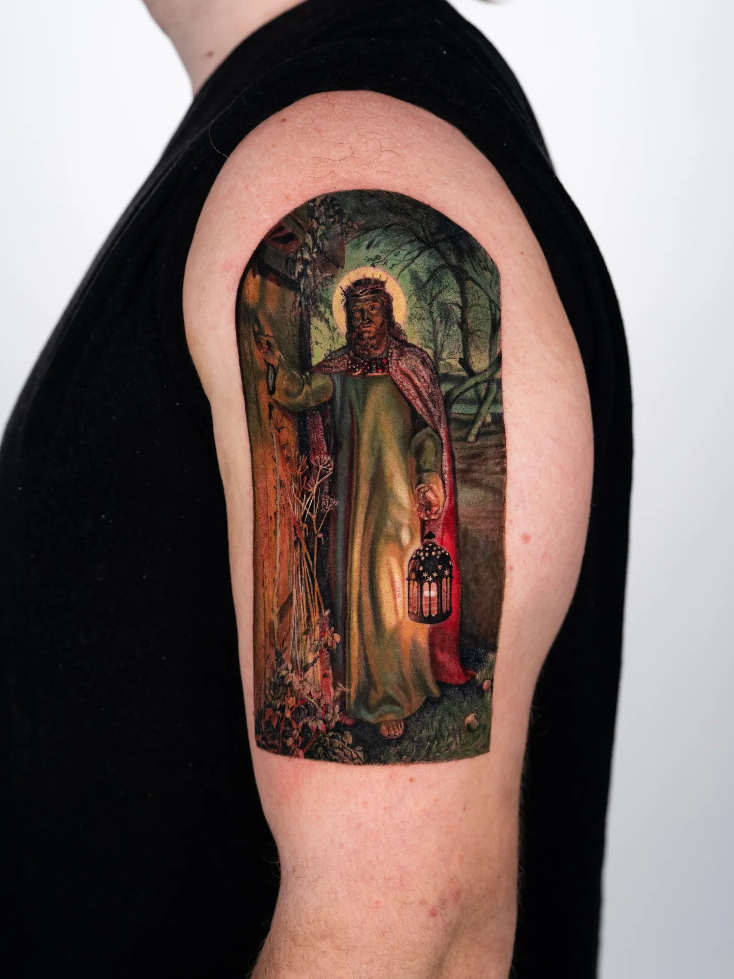 Tattoo of a religious figure holding a lantern on the upper arm