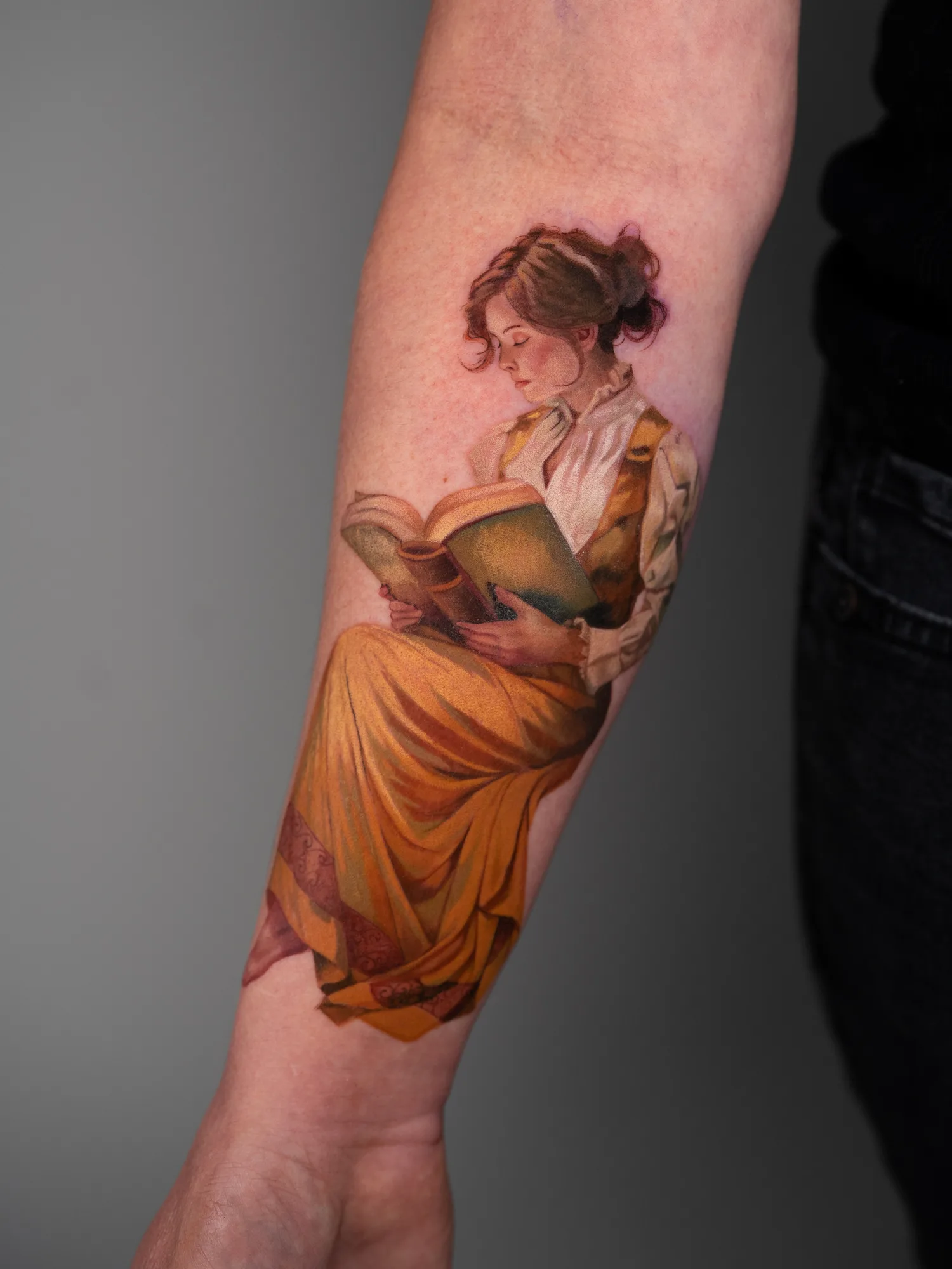 Tattoo of a woman in period clothing reading a book, placed on forearm.