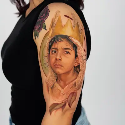 Tattoo of a child in a crown on woman's upper arm.