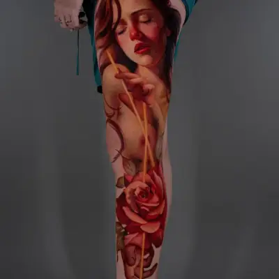Tattoo of a woman's face with closed eyes and a red rose on the thigh.
