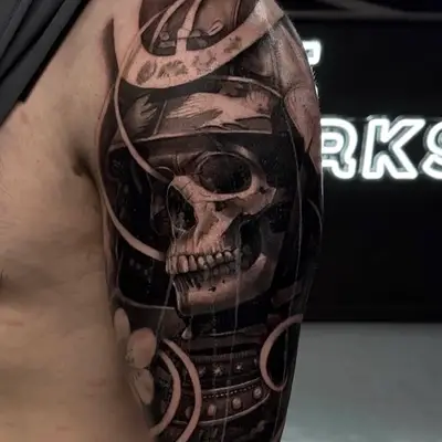 Realistic skull tattoo on upper arm with helmet and abstract elements.