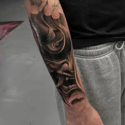 Abstract black and grey tattoo on forearm with swirling patterns.