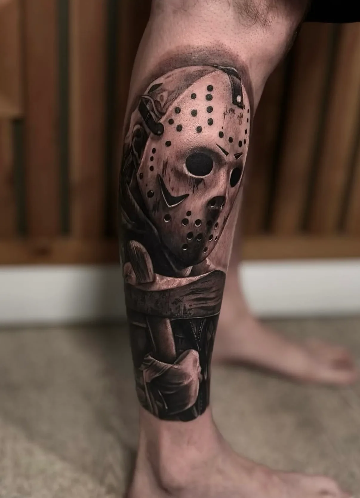 Realistic tattoo of a hockey mask character on a calf.