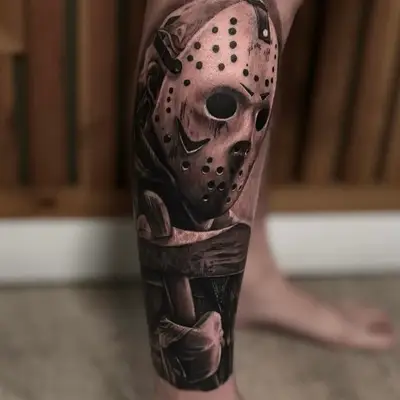 Realistic tattoo of a hockey mask character on a calf.