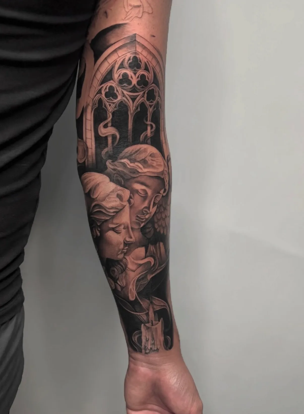 Black and grey tattoo of two angelic figures with candle and stained glass design.