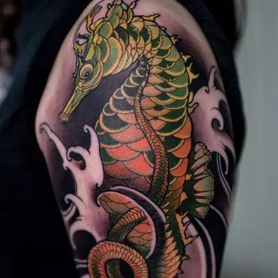 Color neo-traditional seahorse on the upper arm and shoulder, its scales in green, gold and orange with a curled tail, framed by white-capped black waves.
