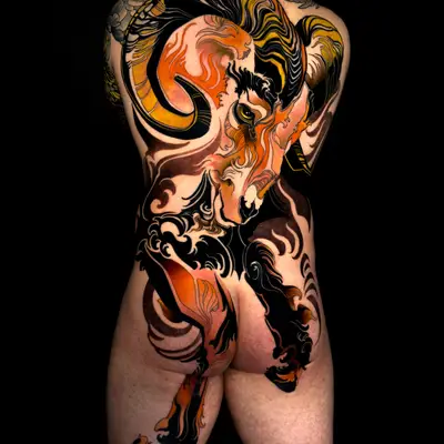 Full back tattoo of a ram in orange, gold and black, its curling horns across the shoulder blades and head bowed down the spine, with its legs running over the hips onto the backs of the thighs, against black ornamental smoke shapes.