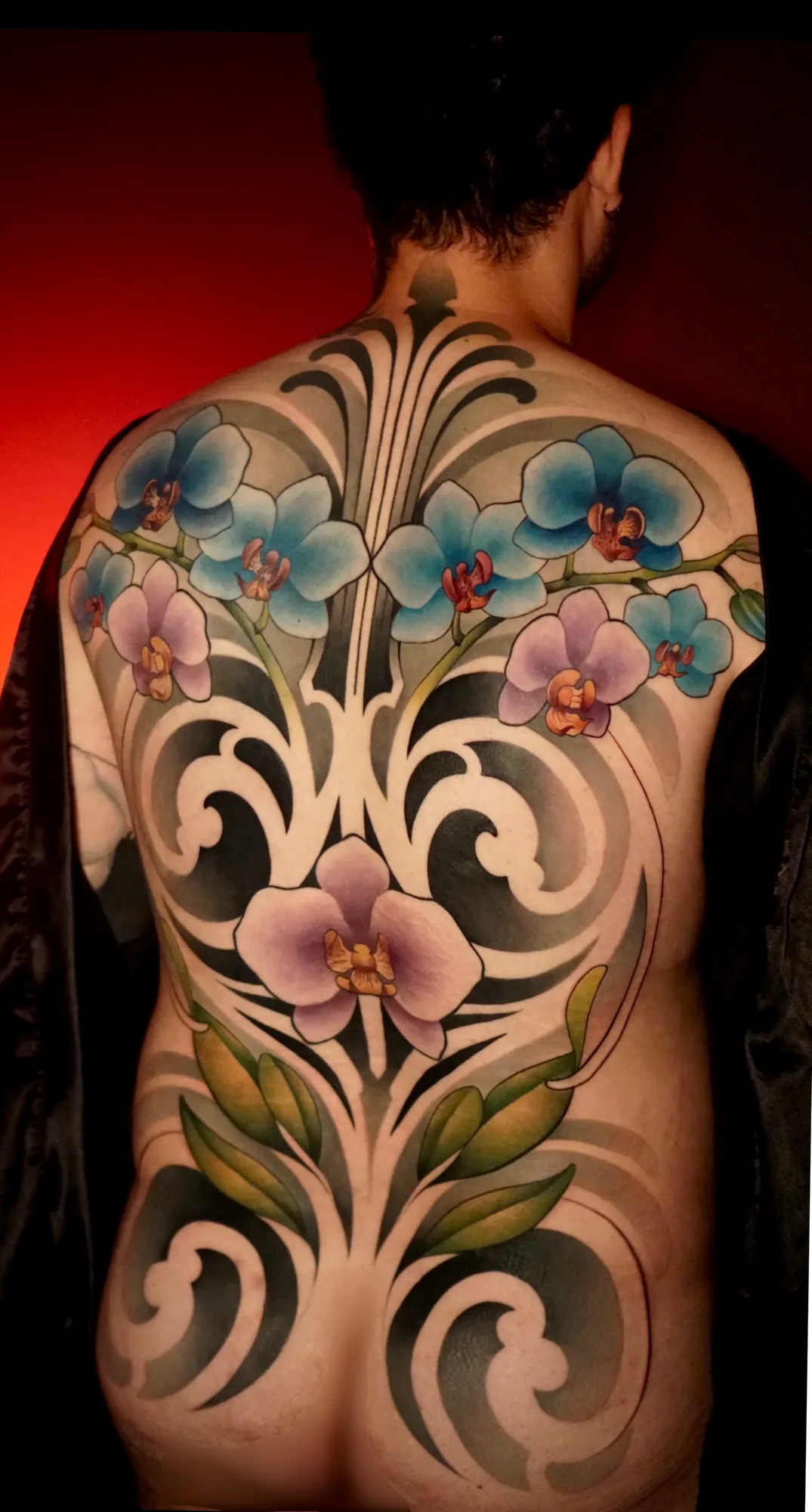 Back tattoo with vibrant orchids and black ornamental swirls.