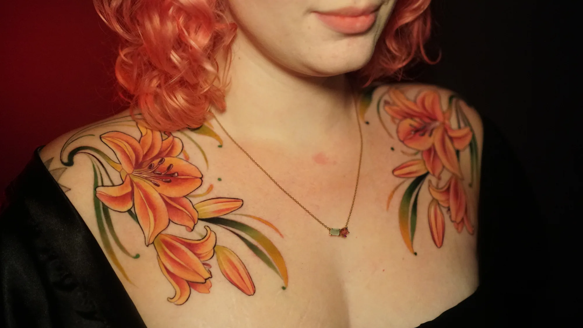 Two orange lily tattoos on woman's shoulders.