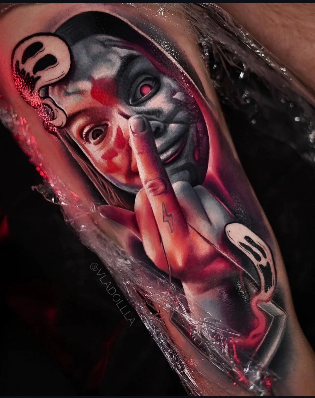 Color realism portrait tattoo: a grinning young woman raising her middle finger, with red washes and white graffiti-style smiley faces around her, photographed fresh under wrap.