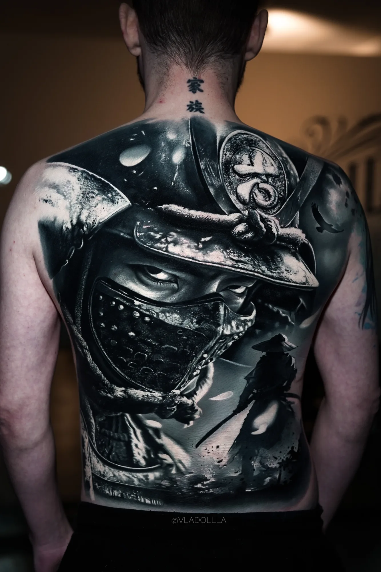 Black and grey realism full back piece of an armored samurai in a mempo mask, with a straw-hat ronin silhouette below.