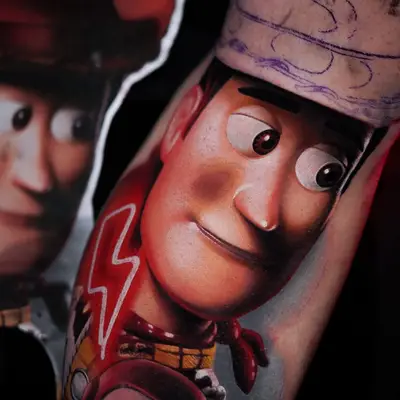 Color realism upper arm tattoo of Woody from Toy Story with a red lightning bolt, stencil for the next section visible above.