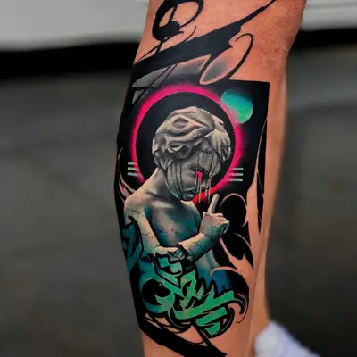 Tattoo on the calf: a grey marble cherub raising a finger to its lips inside a pink ring, with teal graffiti lettering below and sweeping black brushstroke calligraphy around it.