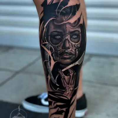 Black and grey tattoo on the calf: a woman's face half turned to skull with pale eyes, a skeletal hand rising beneath it, and bold black calligraphy strokes cutting around the portrait.