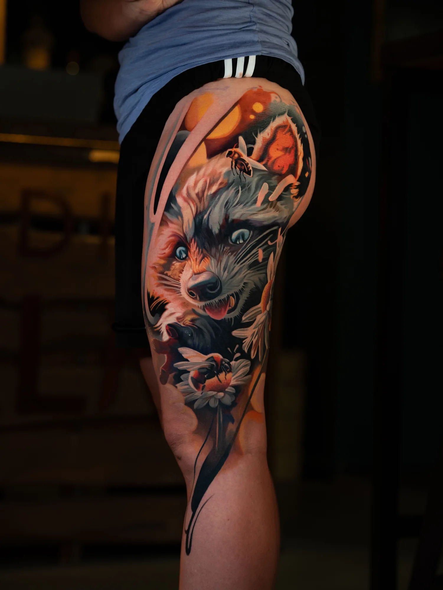 Color realism tattoo of a raccoon and a bee on an outer thigh