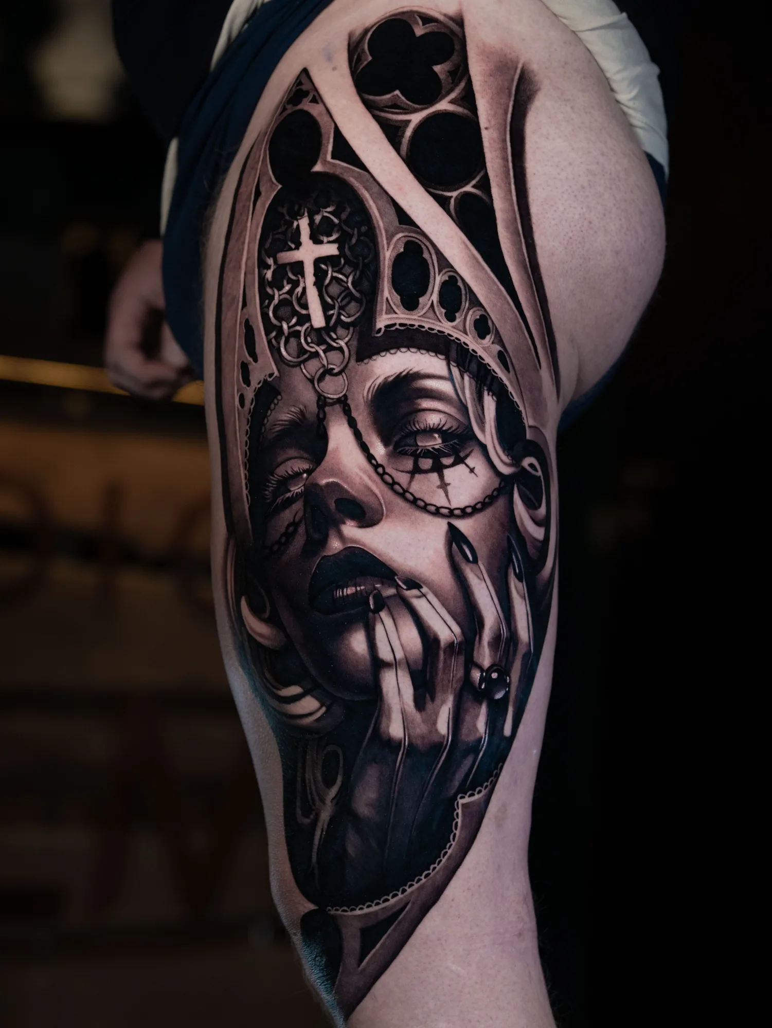 Black and grey realism tattoo of a woman framed by a gothic window on a thigh